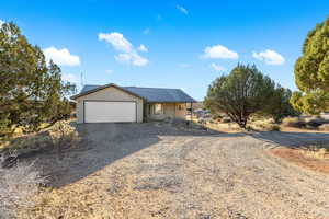 View of front of property featuring gravel driveway, a garage, and a metal roof