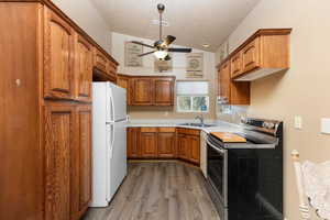 Kitchen featuring stainless steel electric range oven, brown cabinetry, freestanding refrigerator, wood finished floors, and lofted ceiling