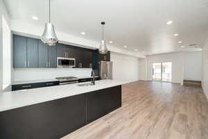 Kitchen with light countertops, backsplash, appliances with stainless steel finishes, light wood-style floors, and pendant lighting