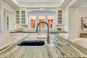 Detailed view of ornamental molding, dark stone counters, white cabinetry, and glass insert cabinets