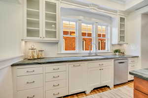 Kitchen featuring tasteful backsplash, dark stone counters, dishwasher, white cabinets, and ornamental molding