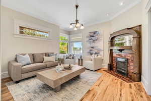 Living area featuring wood finished floors, ornamental molding, a chandelier, and a brick fireplace