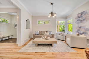 Living area with crown molding, plenty of natural light, a chandelier, and wood finished floors