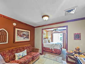 Bedroom featuring a textured ceiling, ornamental molding, tile patterned floors, and a textured wall