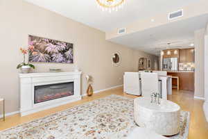 Living room with light wood-type flooring, a glass covered fireplace, recessed lighting, and a chandelier