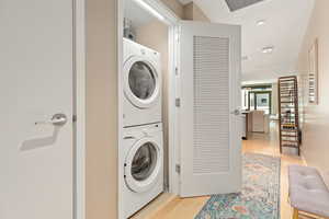 Washroom with stacked washer / drying machine, light wood finished floors, and recessed lighting