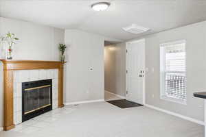 Unfurnished living room featuring a textured ceiling, carpet, and a tile fireplace
