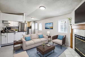 Living area featuring light tile patterned floors, a tiled fireplace, lofted ceiling, and a textured ceiling
