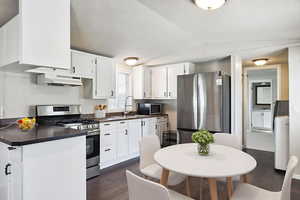 Kitchen with appliances with stainless steel finishes, dark wood-style flooring, white cabinetry, dark countertops, and vaulted ceiling