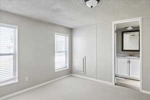 Unfurnished bedroom featuring light colored carpet, a textured ceiling, and ensuite bathroom