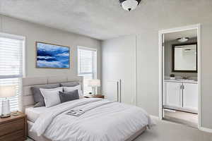 Bedroom with a textured ceiling, light colored carpet, and ensuite bath