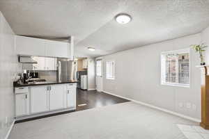 Kitchen featuring washer and dryer, dark countertops, freestanding refrigerator, a textured ceiling, and white cabinetry