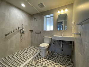 Primary bath featuring roll-in tiled shower, tile walls, recessed lighting, and tile patterned heated flooring