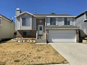 Split foyer home featuring brick siding, double garage, a chimney, driveway, and a front yard