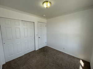 Unfurnished 2nd bedroom with dark colored carpet, ornamental molding, and a closet