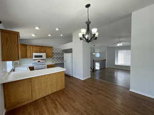 Kitchen with vaulted ceiling, open floor plan, white appliances, a ceiling fan, and a peninsula