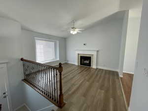 Unfurnished living room with a ceiling fan, lofted ceiling, wood finished floors, and a fireplace