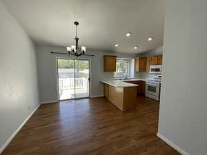 Kitchen featuring a chandelier, a peninsula, white appliances, dark wood finished floors, and light countertops