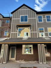 View of front of house featuring a patio, brick siding, and roof with shingles