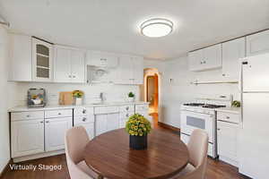 Kitchen featuring arched walkways, white appliances, dark wood finished floors, and white cabinets