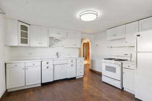 Kitchen with arched walkways, white appliances, white cabinetry, and light countertops
