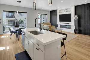 Kitchen featuring light countertops, light wood finished floors, a kitchen bar, white cabinetry, and an island with sink