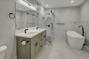 Bathroom featuring tile walls, a marble finish shower, a freestanding tub, double vanity, and a wainscoted wall