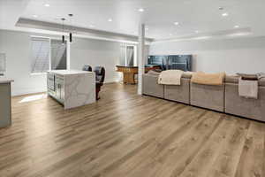 Living area with a tray ceiling, light wood finished floors, and recessed lighting