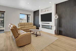Living room with light wood-style floors, a glass covered fireplace, built in shelves, and recessed lighting