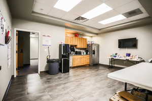 Kitchen featuring a drop ceiling, stainless steel refrigerator with ice dispenser, freestanding refrigerator, and light brown cabinetry