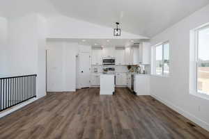 Kitchen with lofted ceiling, dark wood-style floors, white cabinetry, appliances with stainless steel finishes, and a kitchen island