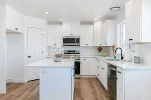 Kitchen featuring stainless steel appliances, a kitchen island, light wood finished floors, white cabinetry, and light countertops