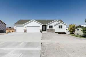 Ranch-style home with an attached garage, stone siding, concrete driveway, and roof with shingles