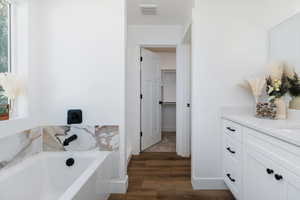 Bathroom featuring vanity, a garden tub, wood finished floors, and a walk in closet