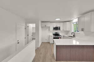 Kitchen featuring light wood-type flooring, a peninsula, stainless steel appliances, light countertops, and white cabinets