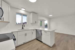 Kitchen with a peninsula, light wood-type flooring, white cabinetry, and light countertops