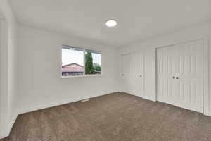Unfurnished bedroom featuring multiple closets and dark carpet