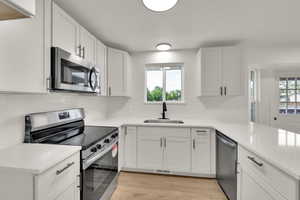 Kitchen with stainless steel appliances, light wood-style flooring, light countertops, white cabinetry, and tasteful backsplash