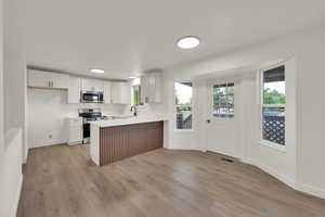 Kitchen with appliances with stainless steel finishes, a peninsula, light wood-style floors, light countertops, and white cabinets