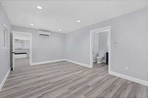Unfurnished bedroom with light wood-style floors, recessed lighting, a wall unit AC, and connected bathroom