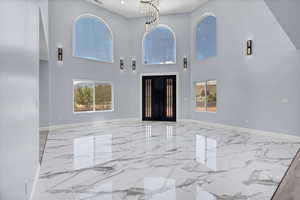 Entryway with light marble finish flooring, a towering ceiling, and a chandelier