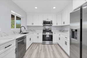 Kitchen with stainless steel appliances, white cabinets, light stone counters, light wood finished floors, and recessed lighting
