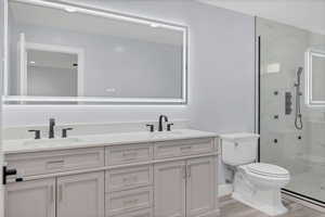 Full bath featuring a marble finish shower, double vanity, and light wood-style floors