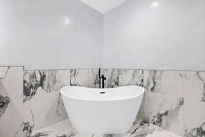 Bathroom featuring a freestanding tub, marble tiled floors, tile walls, and wainscoting