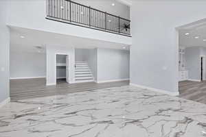 Unfurnished living room with recessed lighting, a high ceiling, light marble finish floors, and stairs