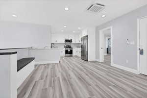 Kitchen featuring white cabinets, light wood-type flooring, recessed lighting, open floor plan, and stainless steel appliances