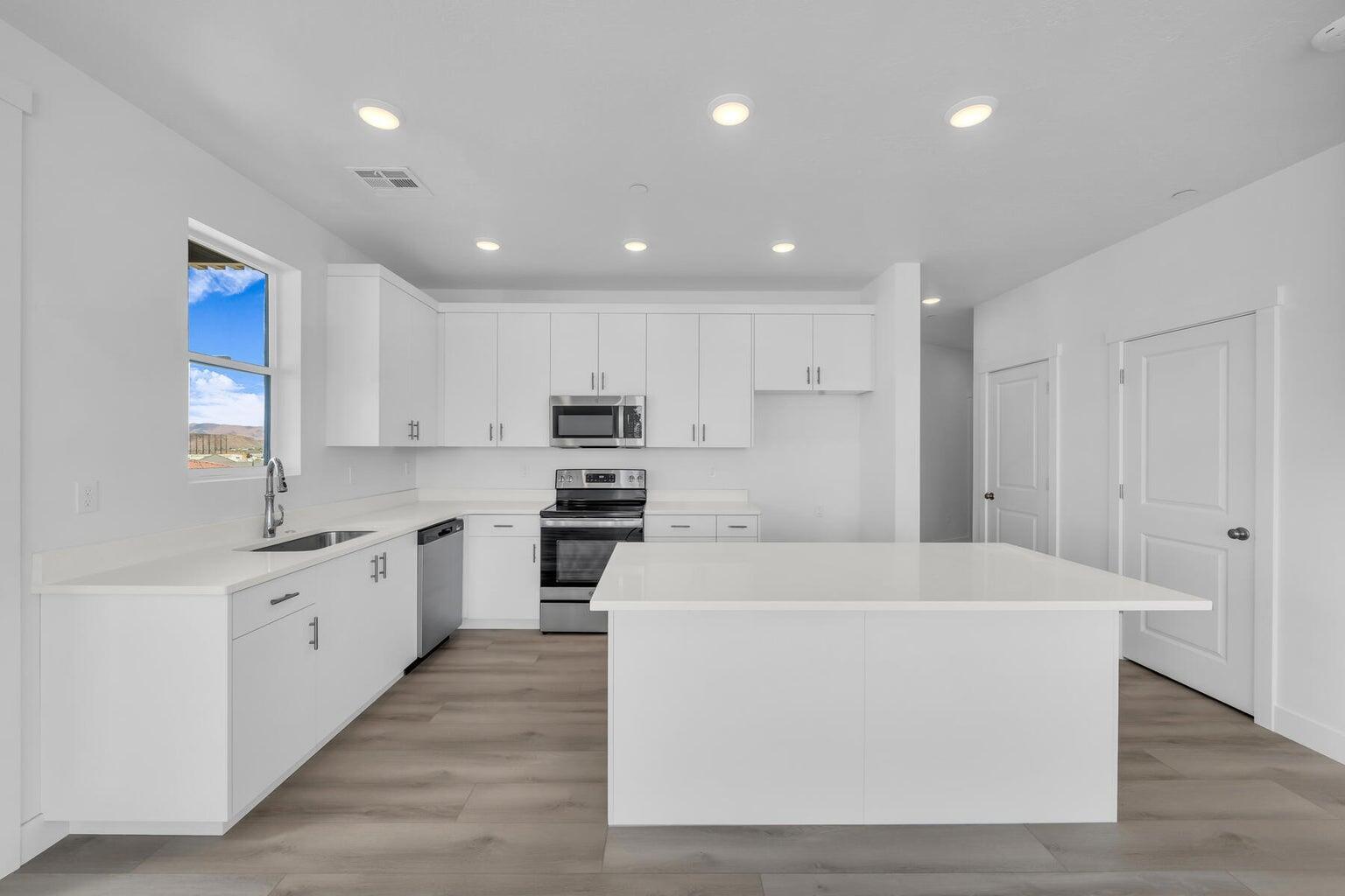 Kitchen with stainless steel appliances, a center island, white cabinetry, light countertops, and light wood-style flooring