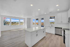 Kitchen with black range, a kitchen island, dishwasher, light wood-type flooring, and light countertops