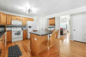 Kitchen featuring decorative backsplash, white appliances, dark countertops, a breakfast bar area, and light wood finished floors