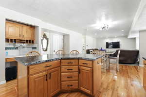 Kitchen featuring light wood-style floors, a textured ceiling, dark countertops, tasteful backsplash, and recessed lighting
